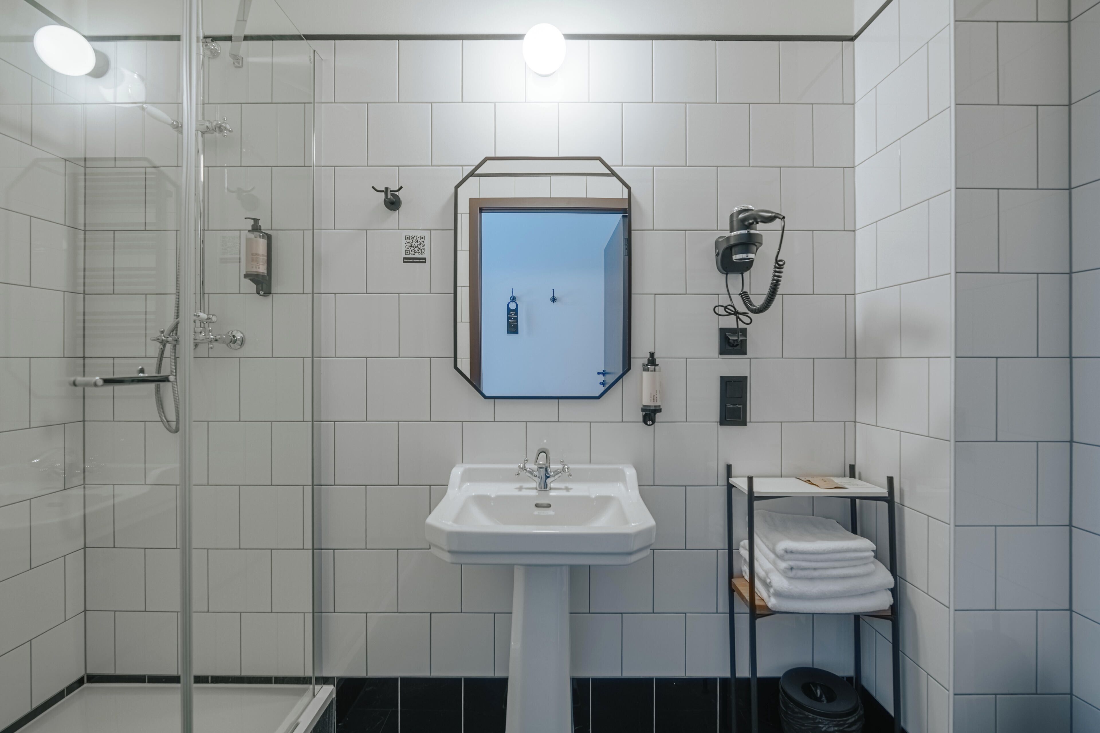 A modern bathroom with a glass shower enclosure, a white sink, and a towel rack.