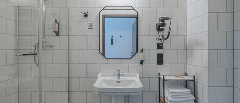 A modern bathroom with a glass shower enclosure, a white sink, and a towel rack.