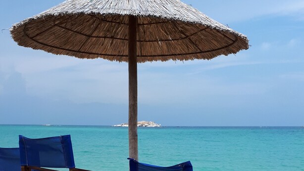 Una playa con sillas de madera y un paraguas de paja.