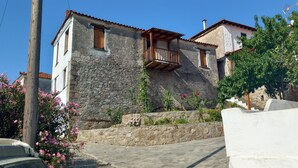 Un edificio de piedra con un balcón, una pared de piedra y flores rosadas.