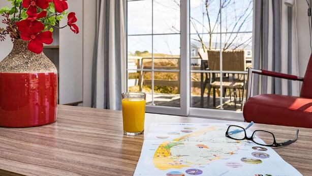 Ett rum med ett träbord, en röd vas med röda blommor, ett glas apelsinjuice, ett par glasögon och en karta över Texas som ligger på bordet.