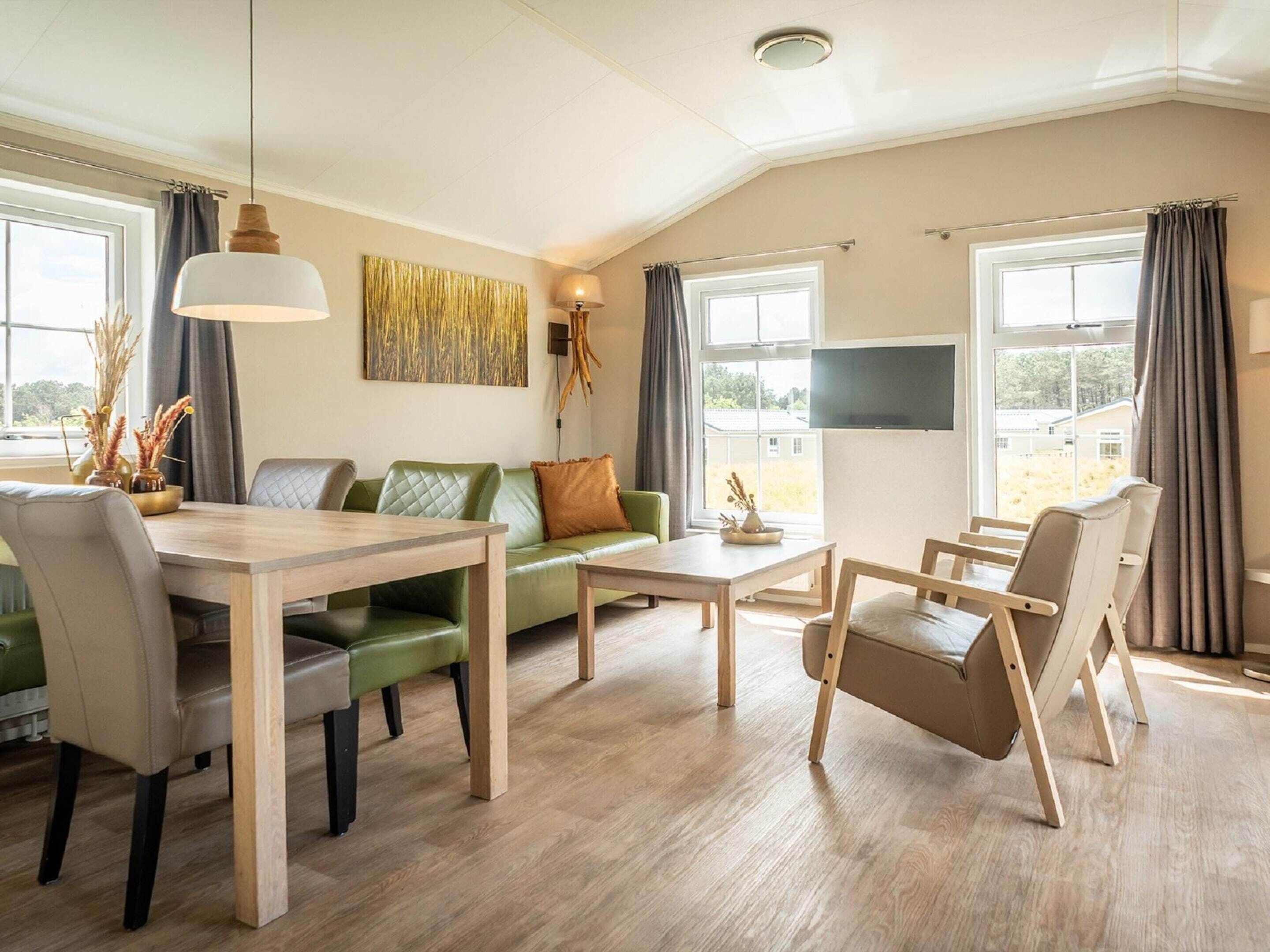 A modern living room with a green sofa, wooden coffee table, and a dining table with chairs.