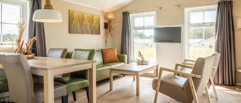 A modern living room with a green sofa, wooden coffee table, and a dining table with chairs.