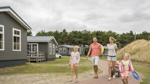 En familj promenerar på en asfalterad stig med ett hus och en gräsyta i bakgrunden.