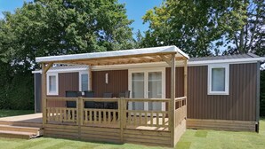 A wooden deck with a covered seating area and a small building with windows. - Comfortable Chalet With Microwave, on a Holiday Park 1 km. From the Beach (Koudekerke)