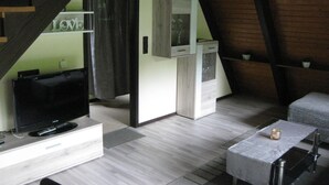 A modern loft-style room with a TV, a small kitchenette, and a cozy seating area. - Wooden Bungalow With a Terrace, in a Wooded Area (Ronshausen)