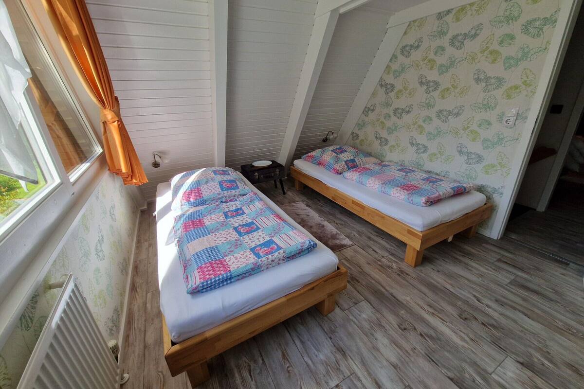 Une petite pièce agréable, dotée de deux lits en bois, d’un radiateur et d’une fenêtre avec des rideaux.
