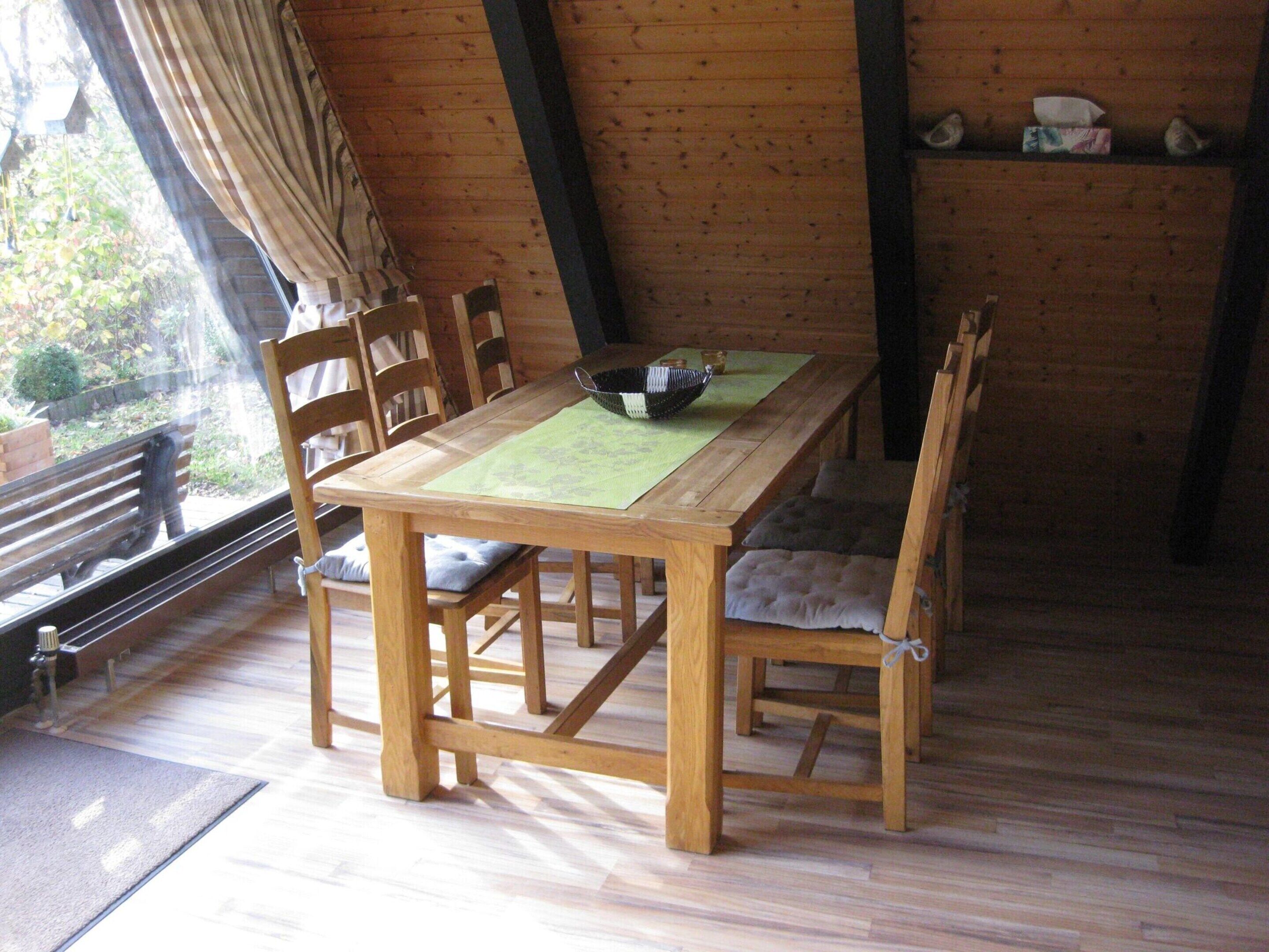 Una mesa de madera con sillas, un mantel individual verde y un tazón.