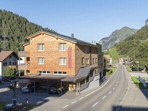 Un hotel de fachada de ladrillo, con una zona de estacionamiento techada y una carretera que conduce a una zona montañosa.