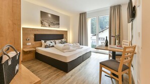 A modern hotel room with a large bed, a wooden headboard, a bedside table, a TV, a dining table with chairs, and a window with curtains. - Majestic Apartment in Klosterle With Sauna on the Arlberg Met Terras (Klösterle am Arlberg)