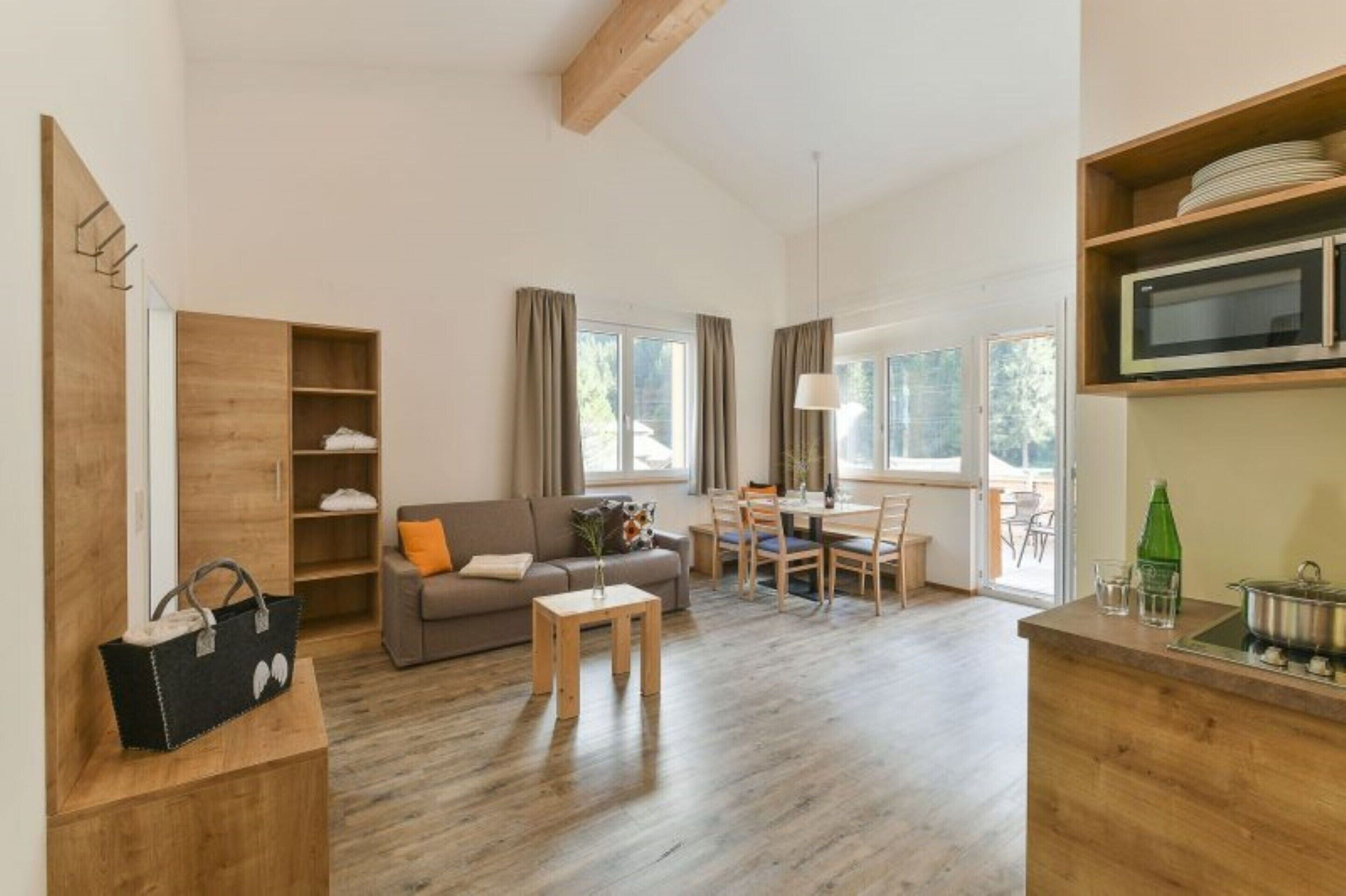 A spacious living area with a sofa, coffee table, and dining table. There is a wooden cabinet with shelves and a microwave on the counter.