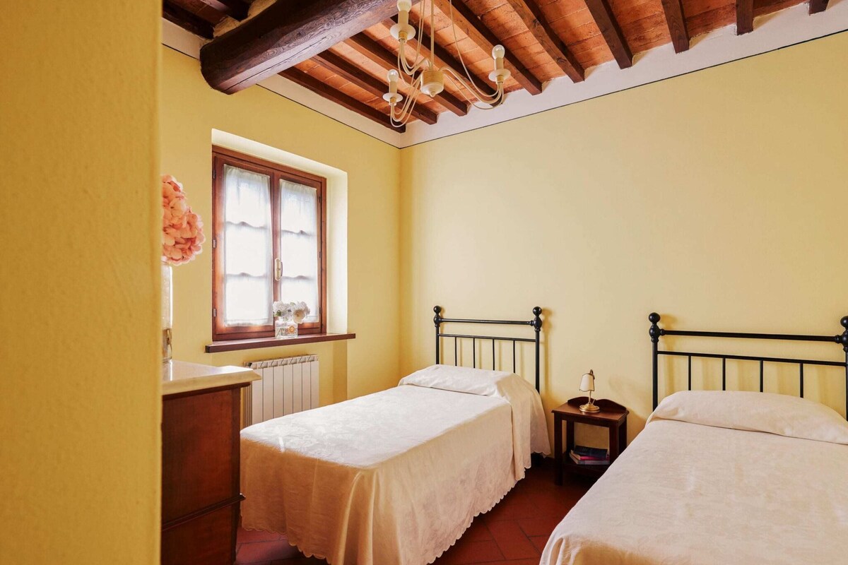 A small, cozy bedroom with two single beds, a wooden dresser, a window with curtains, and a radiator.