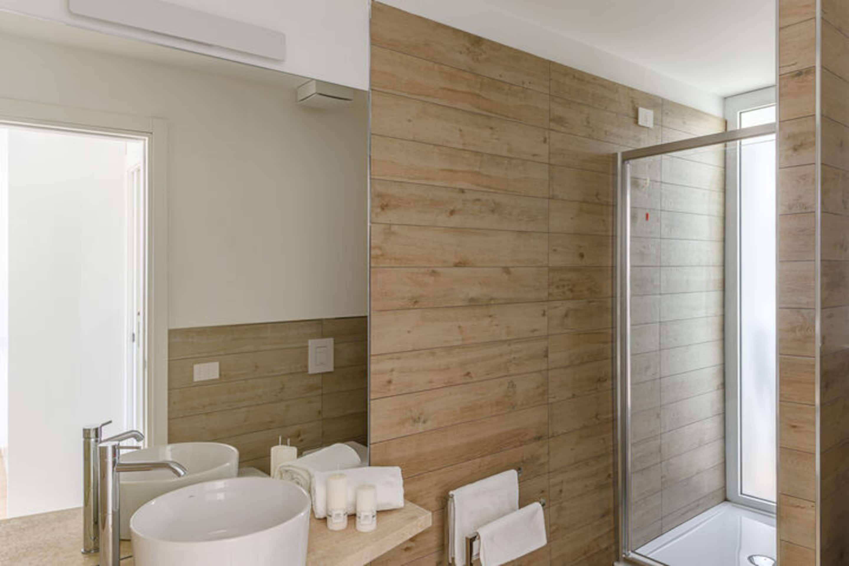 A modern bathroom with a wooden wall, a large sink, a mirror, and a shower enclosure.