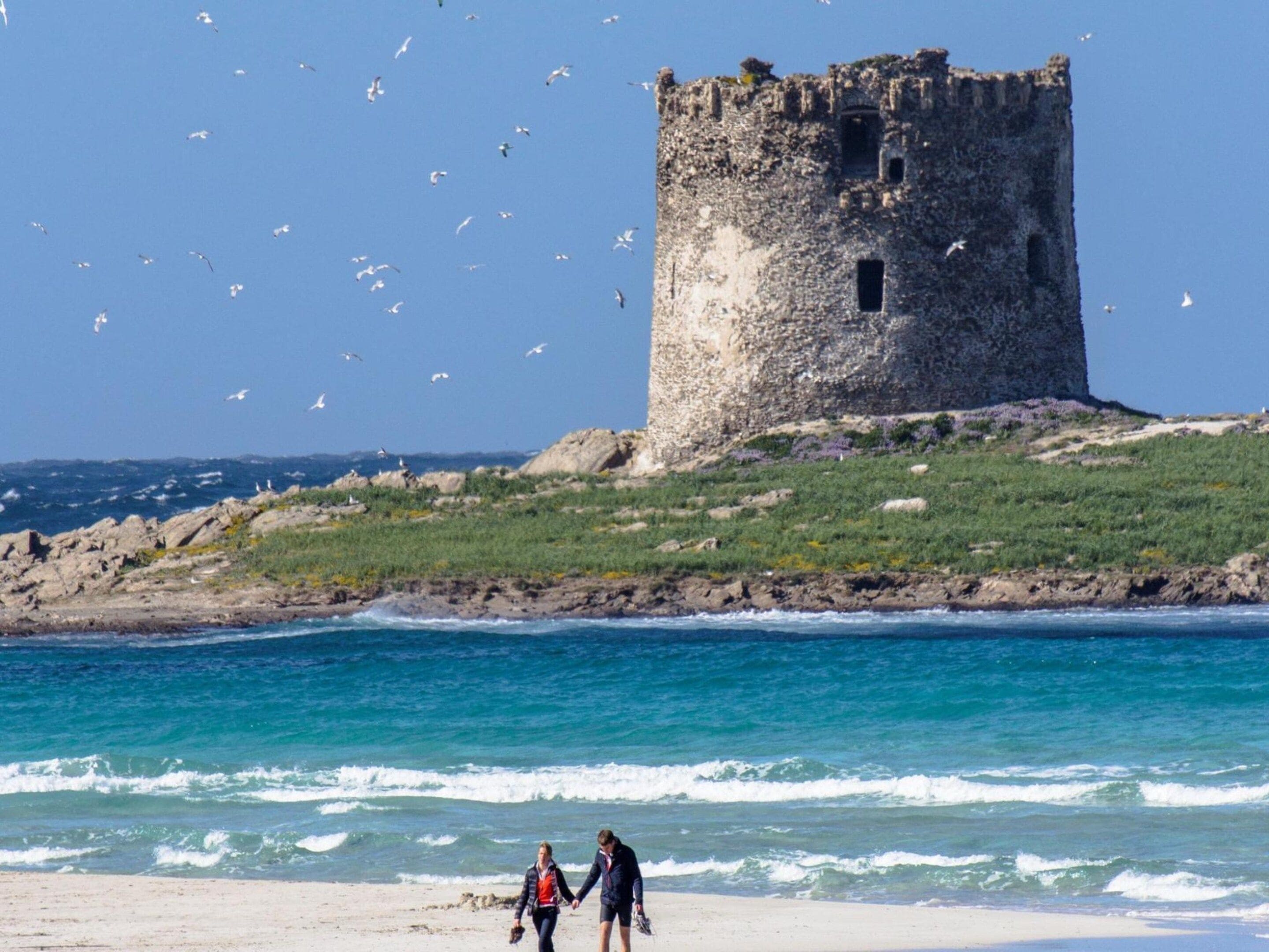 A coastal scene with a stone tower, a sandy beach, and the ocean.