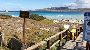 A beach with a wooden boardwalk, a sign indicating 'Libeccio', and a beach access sign with rules. - Residence Capo Falcone, Stintino (Stintino)