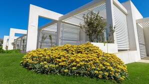 A modern building with white structural elements and a large flower bed in front. - Residence Capo Falcone, Stintino (Stintino)