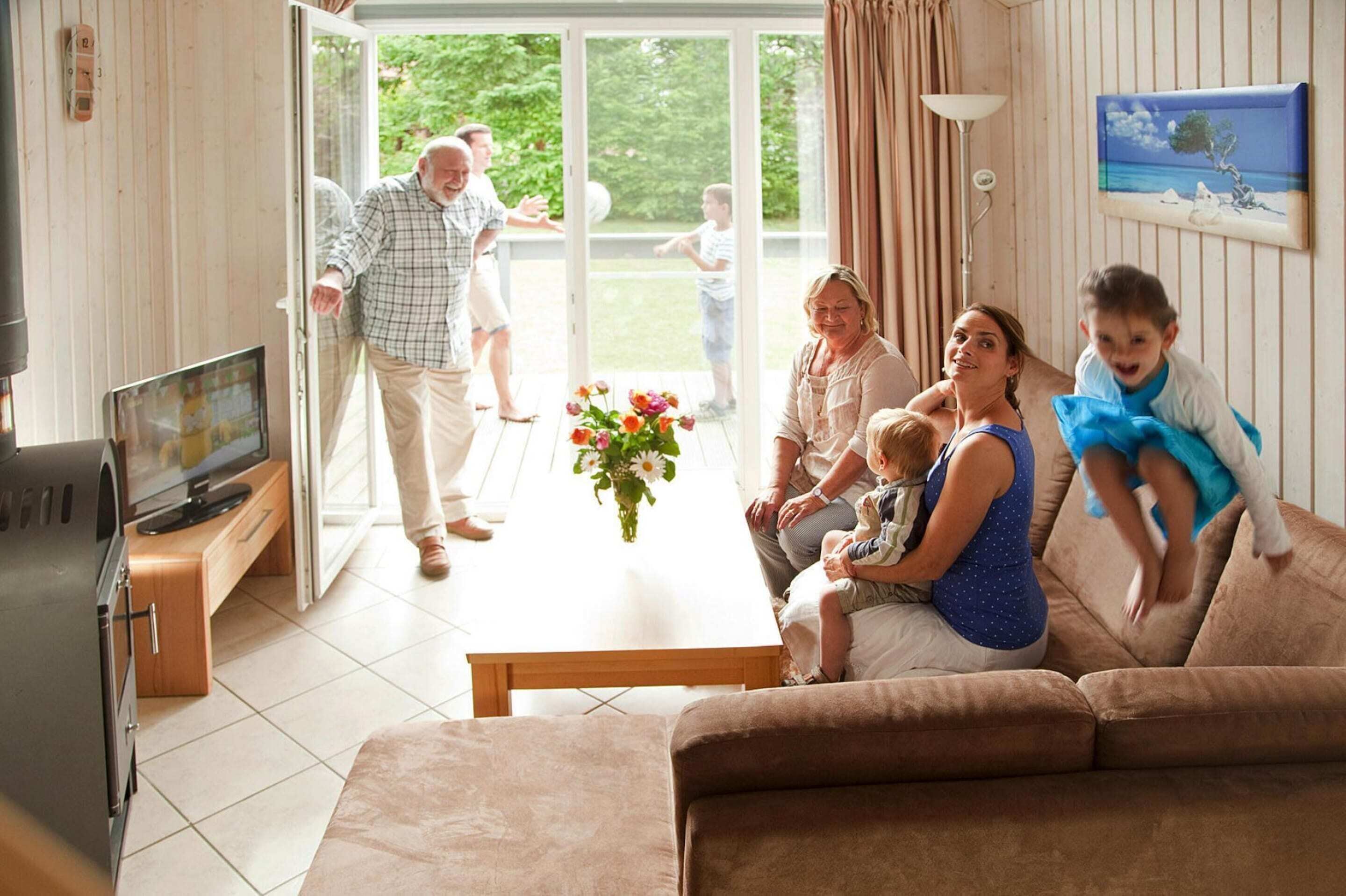 Ein Wohnzimmer mit Fernseher, einem Couchtisch mit Blumen und einer Couch.