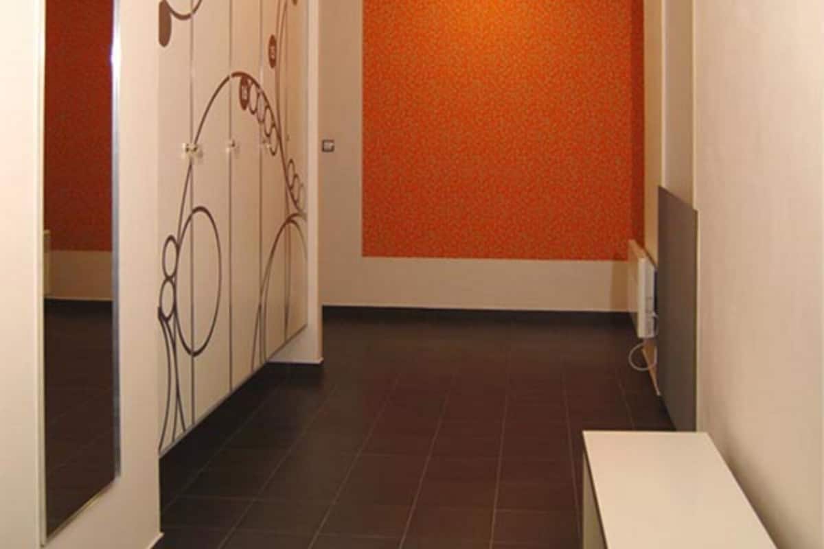 Een gang met een betegelde vloer, een witte bank en een muur met een oranje patroon.