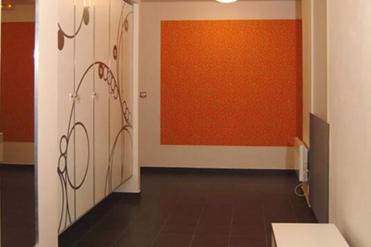 Een gang met een betegelde vloer, een witte deur met een decoratieve handgreep, en een oranje accentmuur.