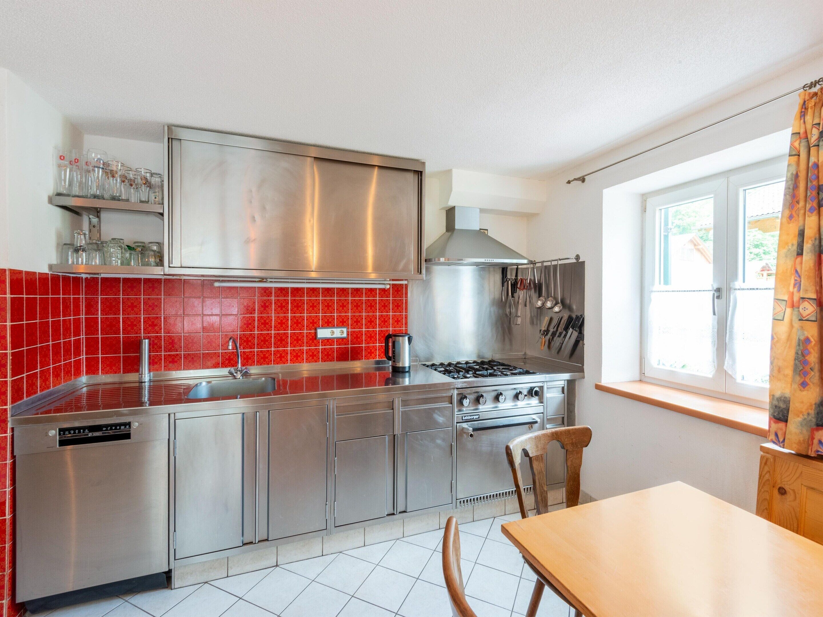 A modern kitchen with stainless steel appliances, a red tiled backsplash, and a window with a view of the outside.