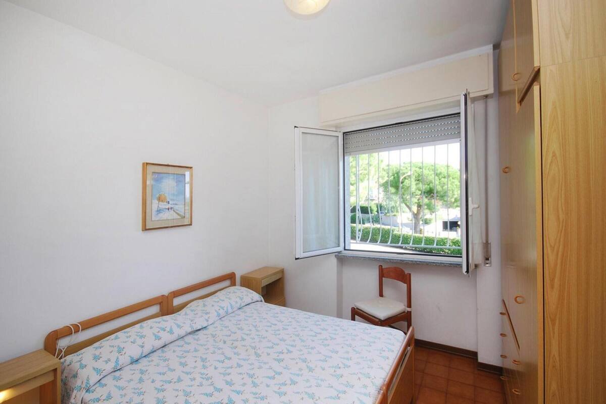 Un dormitorio con una cama, una silla, un ventanal con persianas, una puerta y un cuadro enmarcado en la pared.