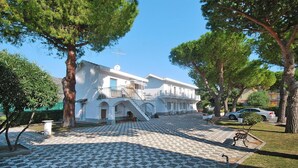 Ένα λευκό κτίριο με μια κεντρική σκάλα, που περιβάλλεται από δέντρα και έναν πλακόστρωτο προαύλιο χώρο.