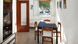 Ένας χώρος τραπεζαρίας με έν α τραπέζι και καρέκλες, μια ξύλινη πόρτα, ένα παράθυρο με θέα σε δέντρα και ένας τοίχος με κορνιζωμένες φωτογραφίες.