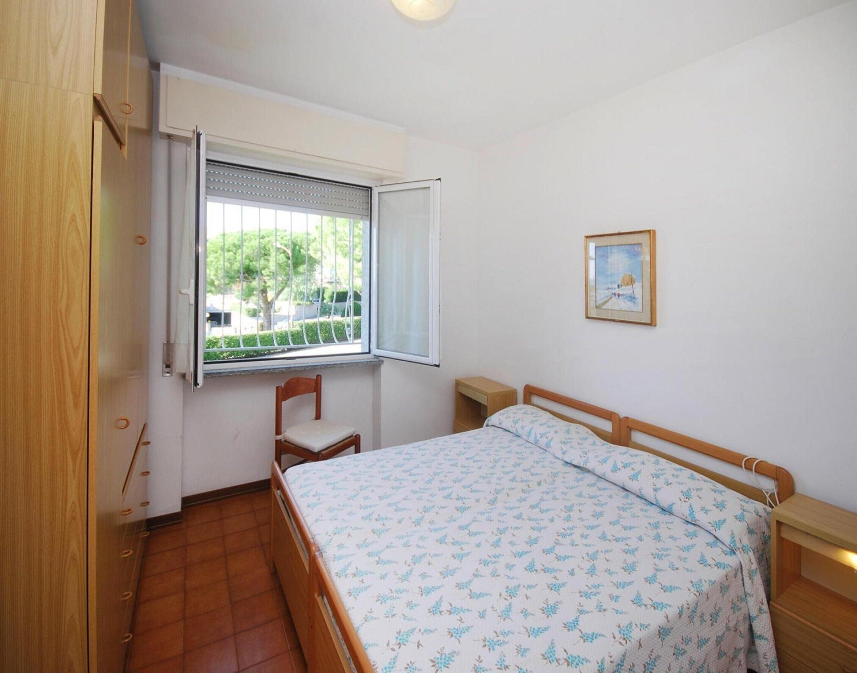 A bedroom with a wooden bed, a window with blinds, a chair, and a small bedside table.