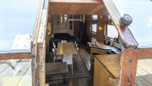 A compact, wooden interior with a dining area, kitchen, and seating space. - Cozy Boat in Merkem Near Lake (Houthulst)