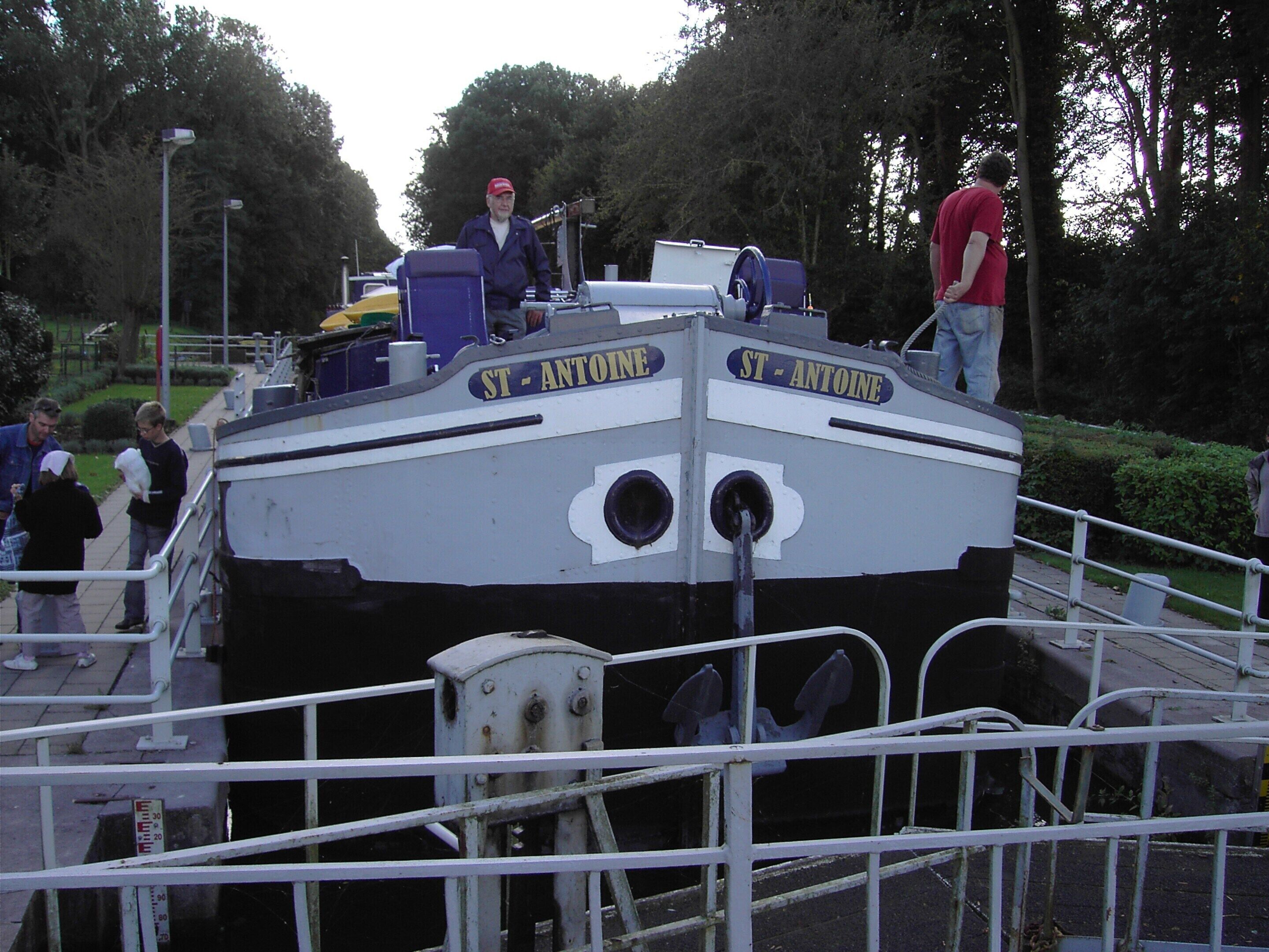 A boat with the name "ST. ANTOINE" on its side, docked at a pier with people around it.