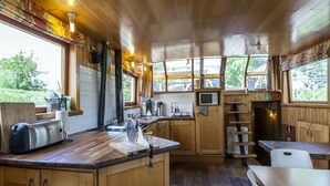 A wooden cabin-style kitchen with a central island, wooden cabinets, a microwave, and a stove. - Cozy Boat in Merkem Near Lake (Houthulst)