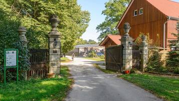 Eine Landstraße führt zu einer Holzbühne mit rotem Dach, umgeben von üppiger Vegetation und Steinsäulen.