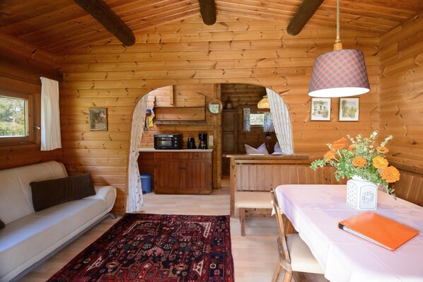A log cabin interior with a sofa, dining table, kitchen area, and a view through an archway.