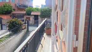 Un balcon avec une rambarde en métal, un pot de fleurs et une vue sur les bâtiments voisins.