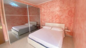 Une chambre à coucher avec un lit, une table de chevet, une commode, un miroir et une porte.
