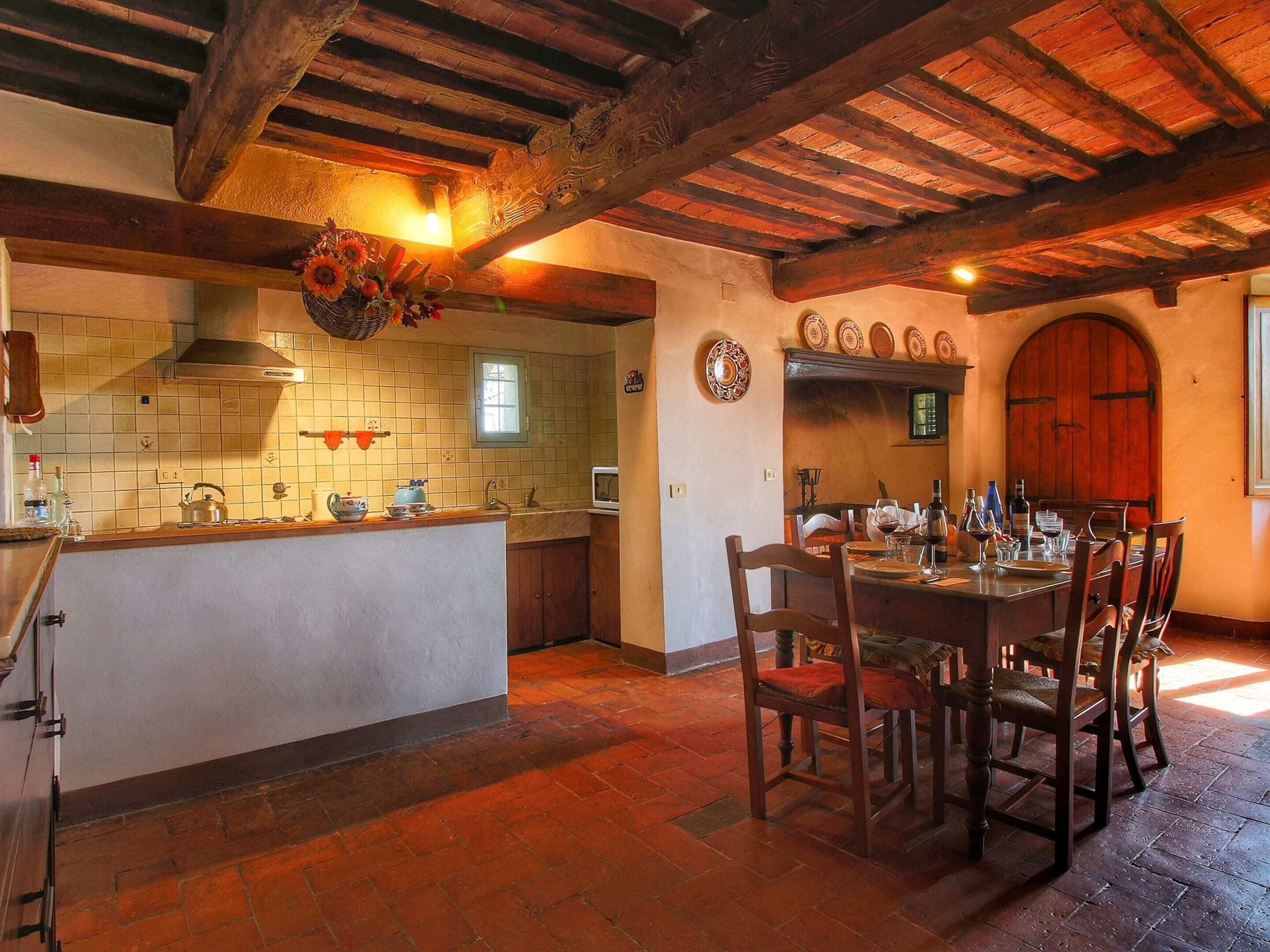 A rustic kitchen with a central island, wooden ceiling beams, and a dining area with a table set for six.