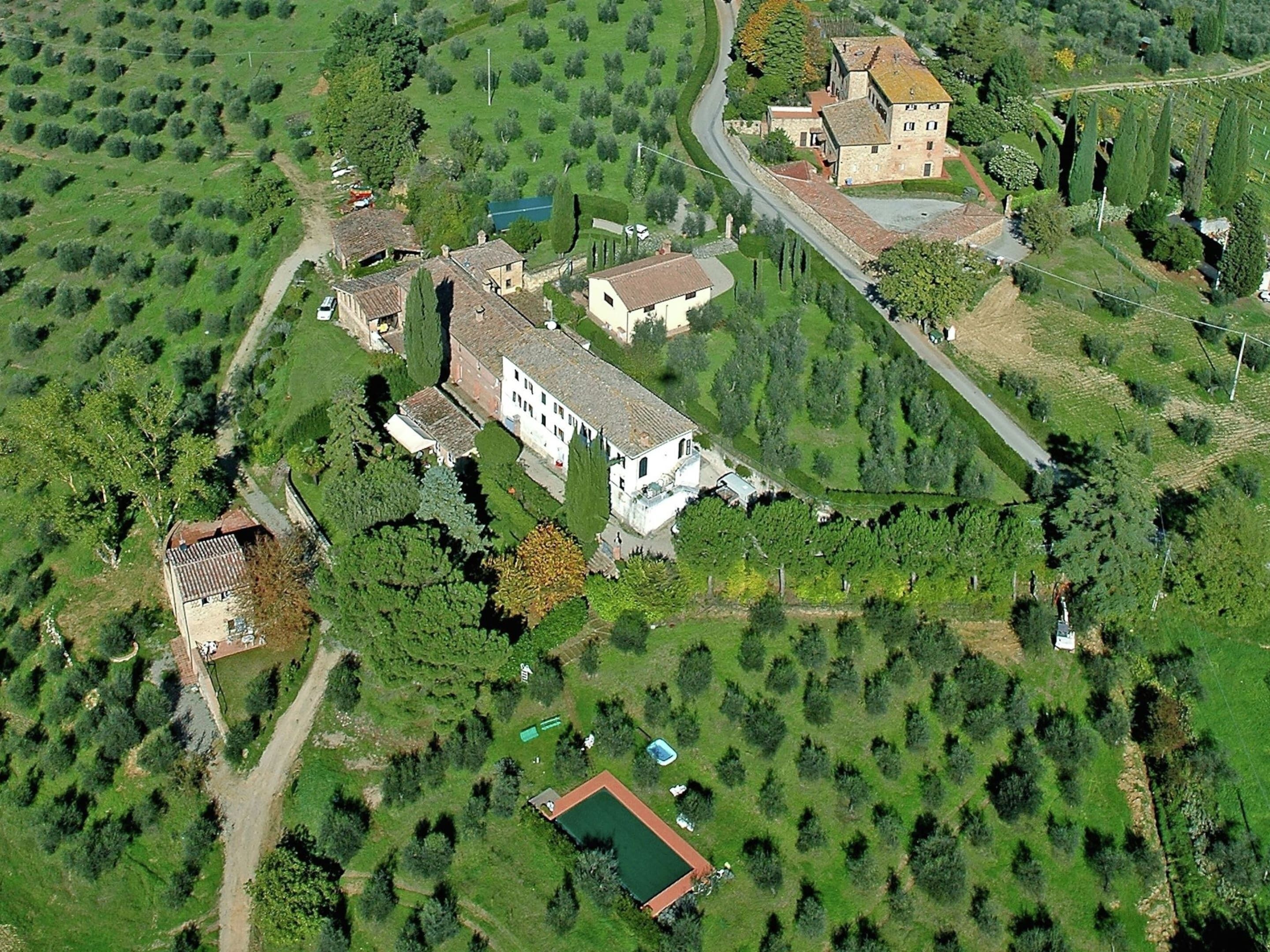 Eine Vogelperspektive eines ländlichen Anwesens mit mehreren Gebäuden, darunter ein großes, weißes Haus mit Ziegeldach, umgeben von üppiger Vegetation und einem kleinen Teich.