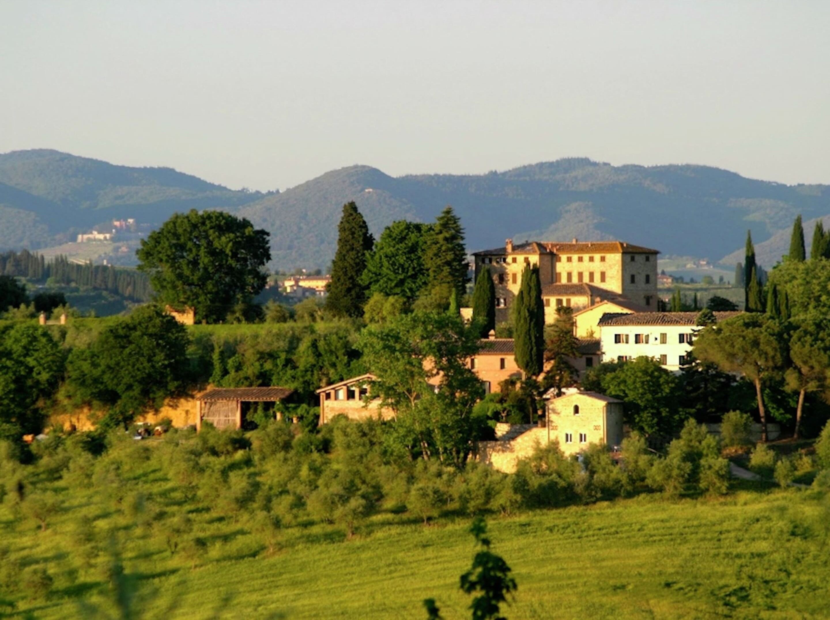 A rural landscape with a large stone building surrounded by trees and fields.
