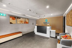 Un área de recepción con diseño moderno, que incluye un mostrador de recepción, un banco y una pantalla montada en la pared.