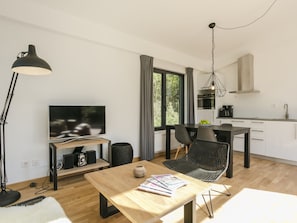 A modern living room with a TV, wooden coffee table, and black chairs. There's a kitchen area with a stove and cabinets. - Furnished Chalet With Dishwasher, Near Almelo (Enter)