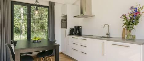 Cocina moderna con armarios blancos, encimera negra y horno empotrado. Hay una mesa con sillas y un florero sobre la encimera.