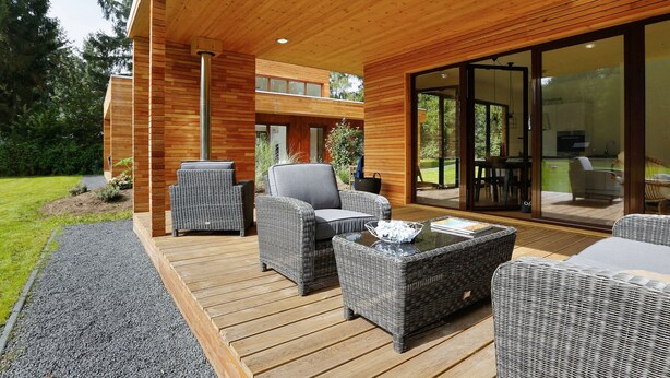 Una terraza moderna al aire libre con mobiliario de mimbre, un portavasos de vidrio que da a un patio, y techo de madera.