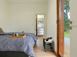 A bedroom with a bed, a bedside table, a chair, and a view of a bathroom and outdoor area. - Furnished Chalet With Dishwasher, Near Almelo (Enter)