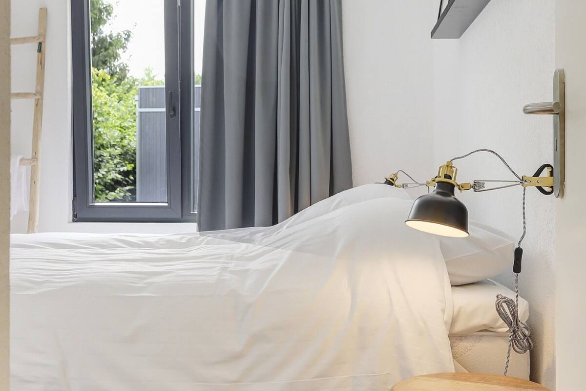 Une chambre à coucher avec un lit, une fenêtre avec des rideaux et une lampe fixée au mur.