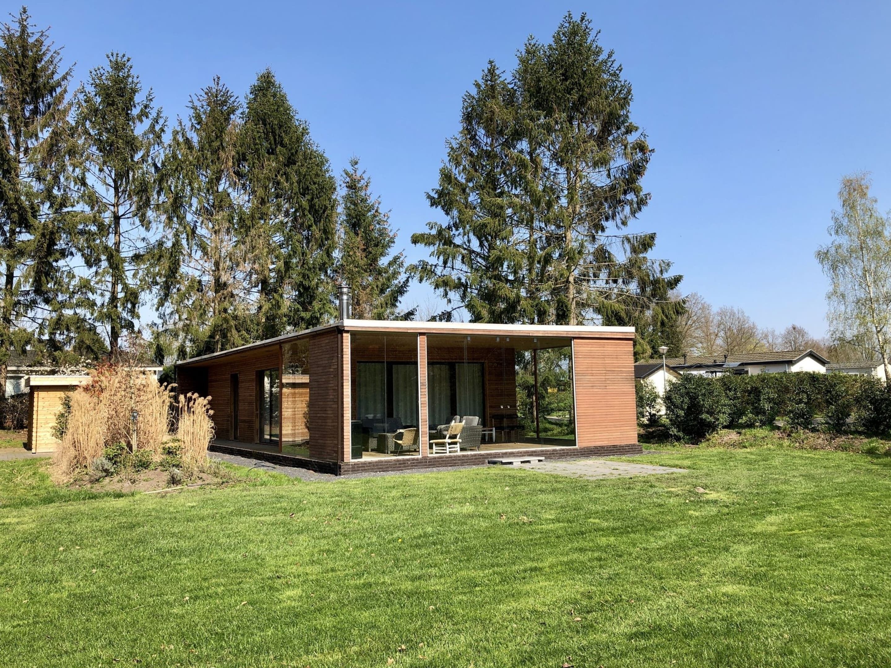 A modern house with a glass-enclosed patio, surrounded by a well-maintained lawn and tall trees.