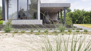 Una casa moderna con ventanas amplias, una silla colgante y un jardín.