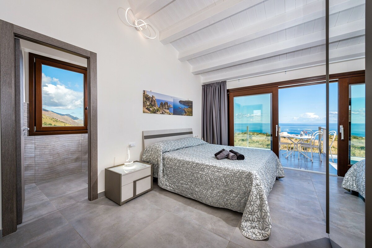A bedroom with a bed, bedside table, and a view of the sea.