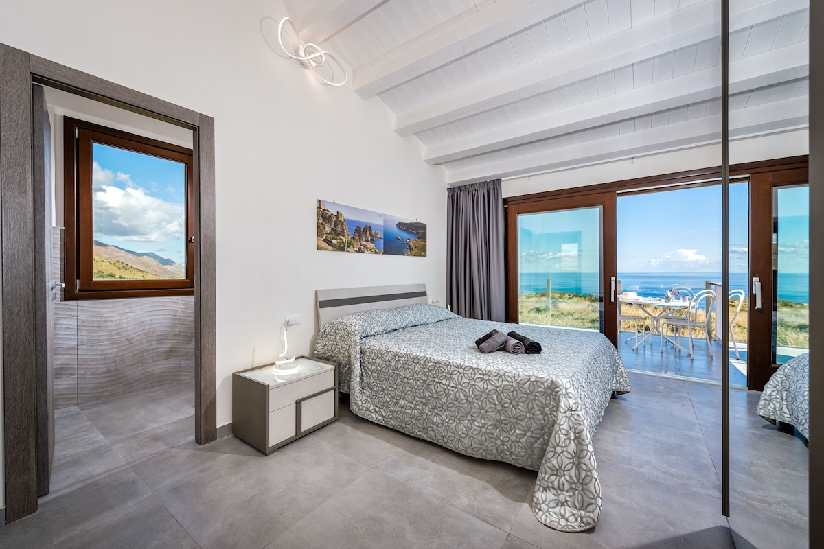 A bedroom with a bed, bedside table, and a view of the sea.