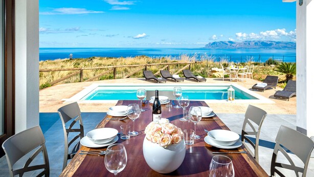 A dining table set for six with a view of the ocean and mountains.