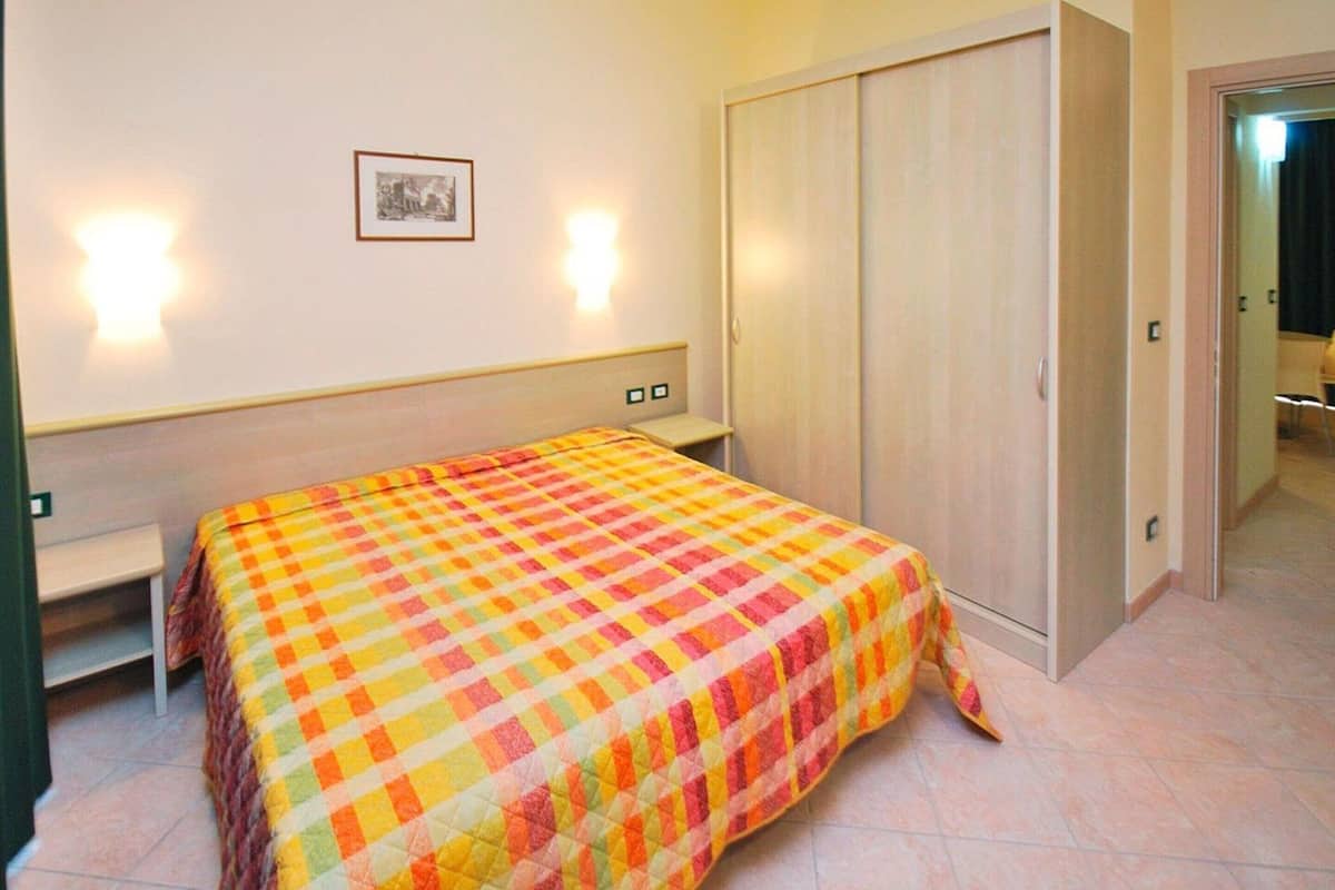 A bedroom with a bed, a wardrobe, a bedside table, and a wall-mounted light.
